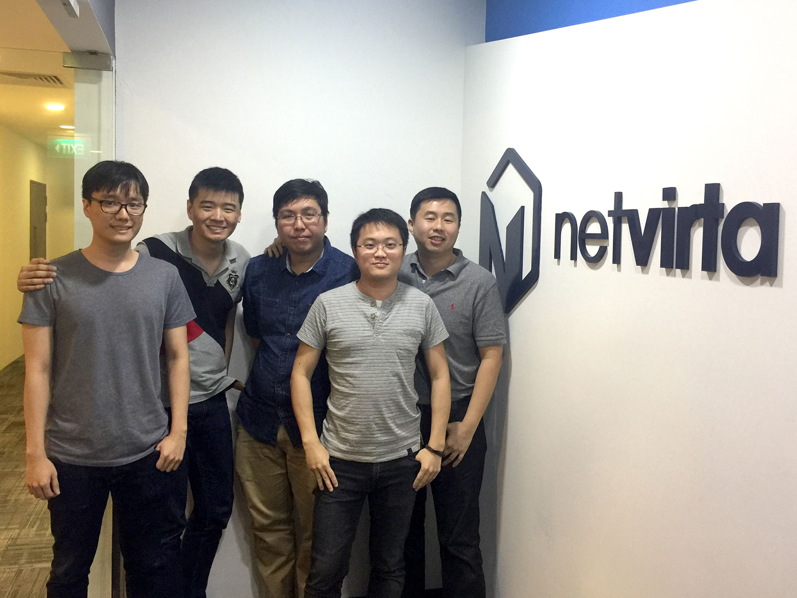 A group of DigiPen Singapore alumni pose next to the logo of Boston-based startup company NetVirta