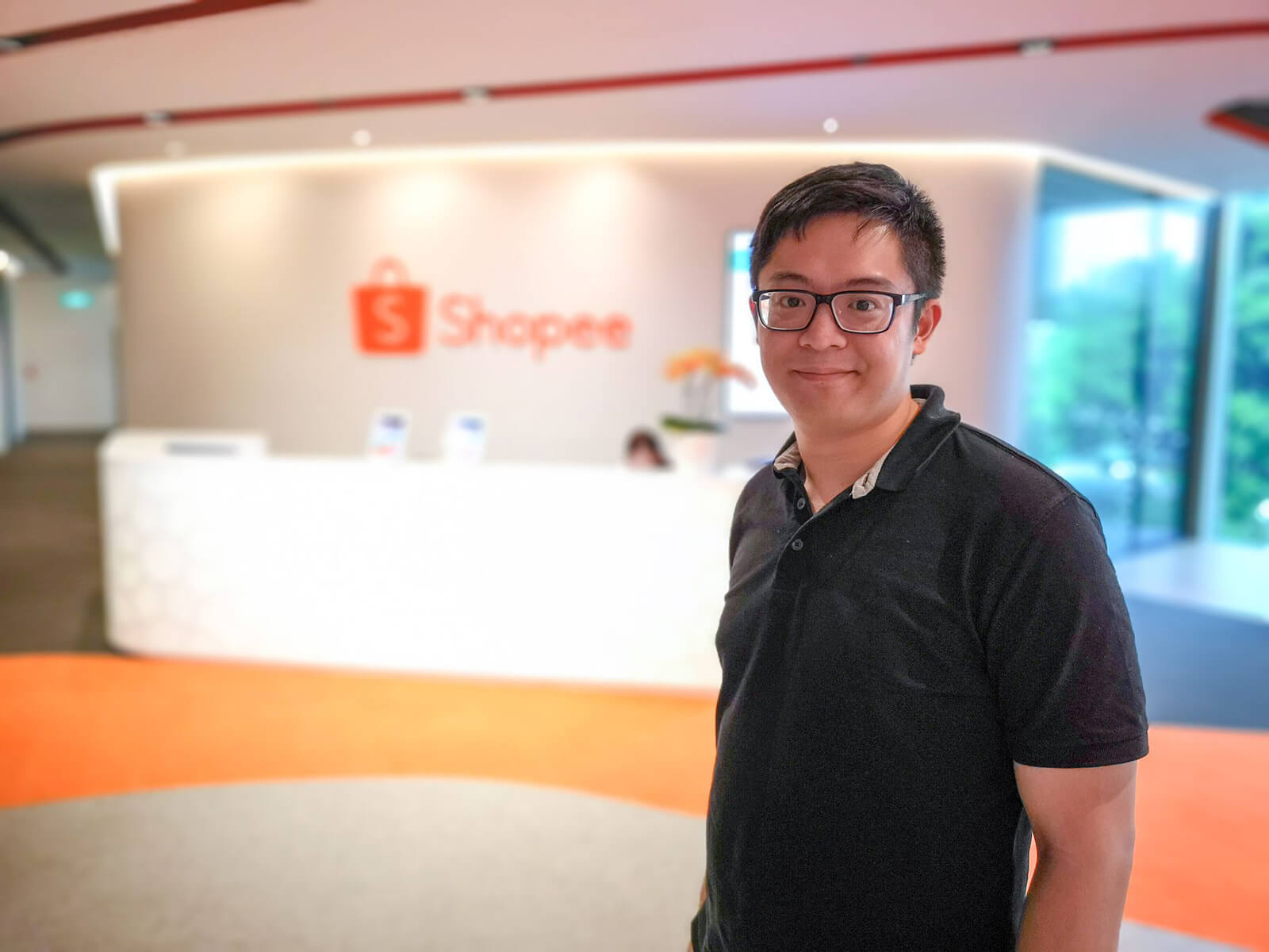 DigiPen (Singapore) alumnus Chester Liew stands in front of a wall adorned with the Shopee logo