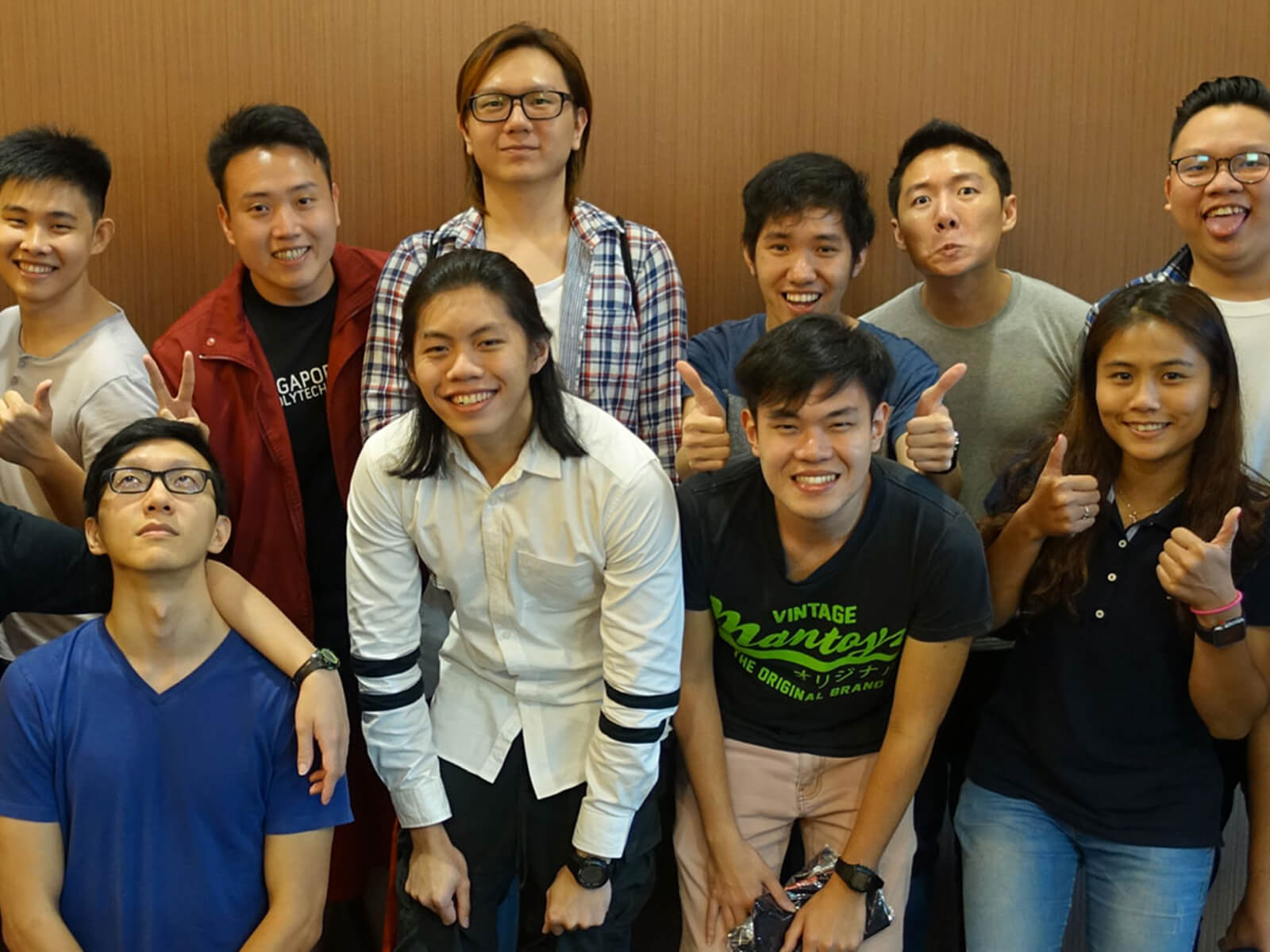 A large group of DigiPen (Singapore) Student Ambassadors smile for the camera, flashing peace and thumbs-up signs