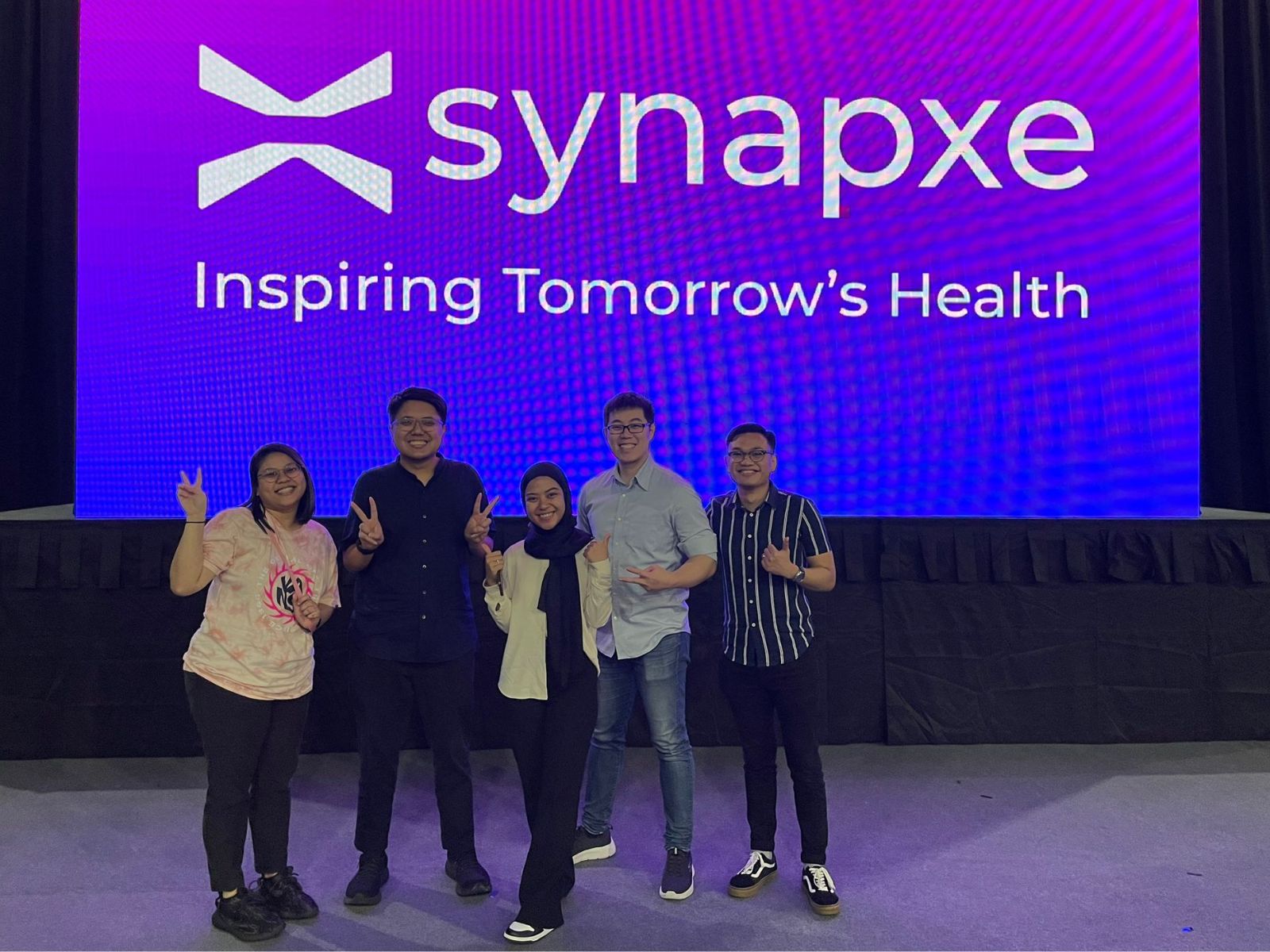 Abdul Aziz poses with 4 other people in front of a Synapxe logo.