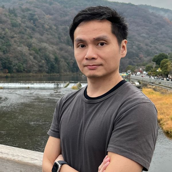 Asian man standing with his arms crossed against a scenic background of a mountain and lake