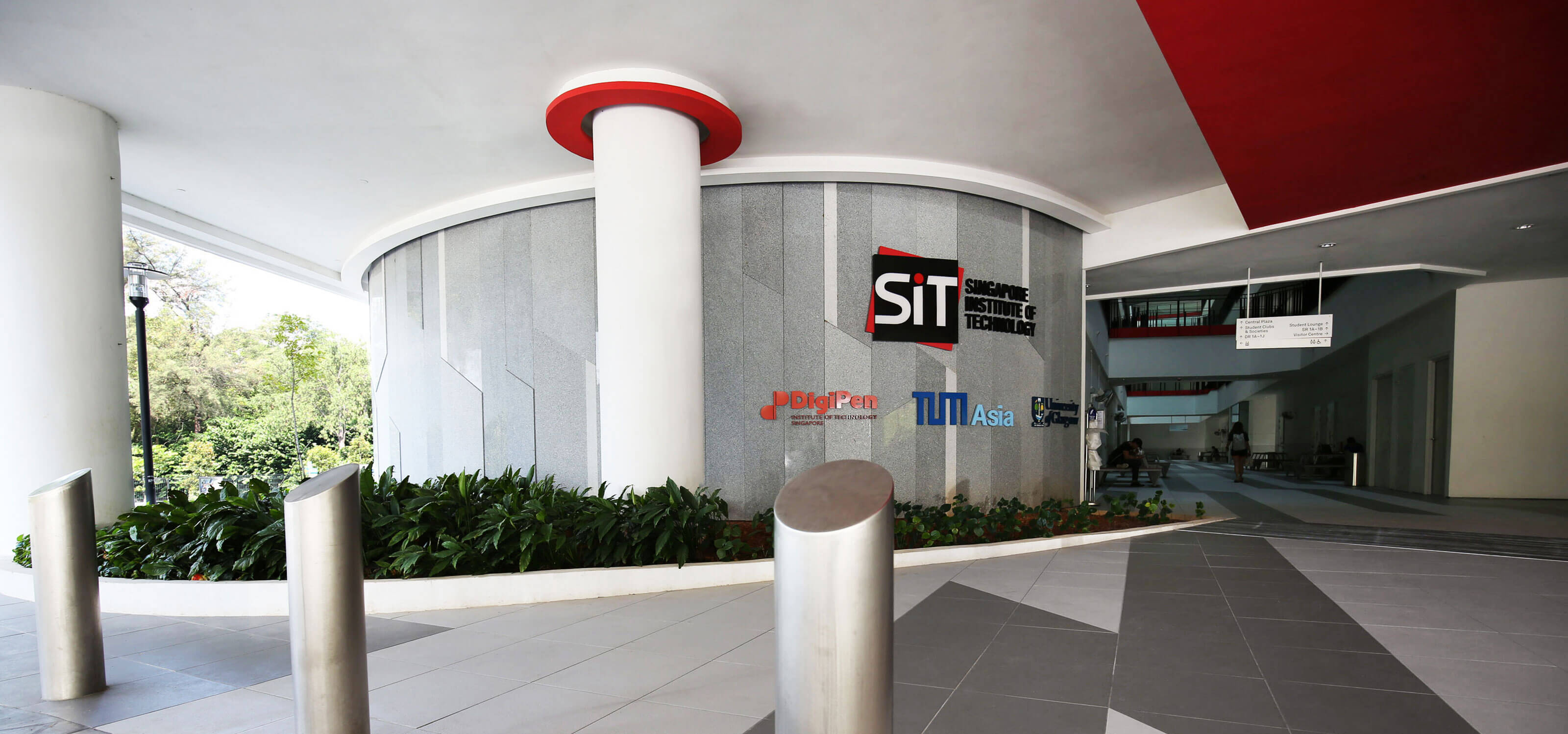 Ground floor exterior of a corporate building with signs for Singapore Institute of Technology, DigiPen, and others.