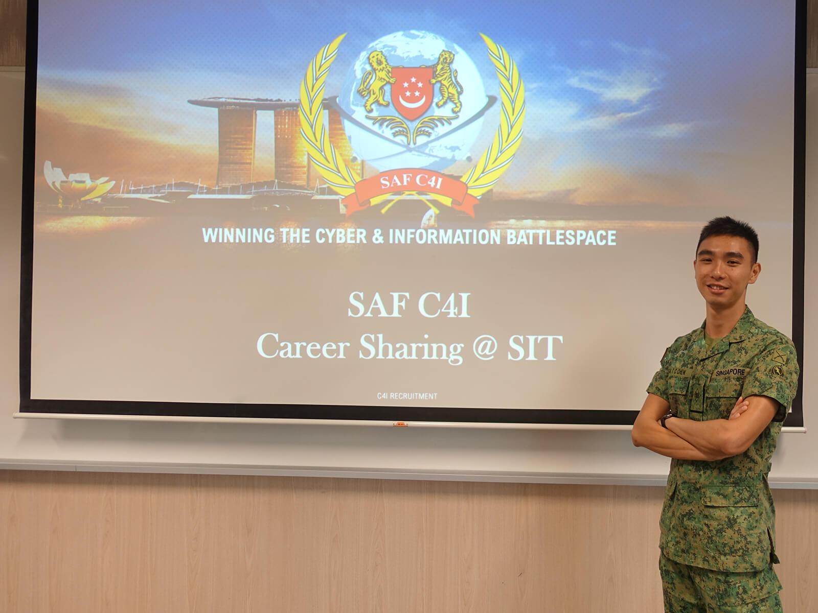 Chew Tee Chin stands in front of a projector screen with the SAF C4I logo.