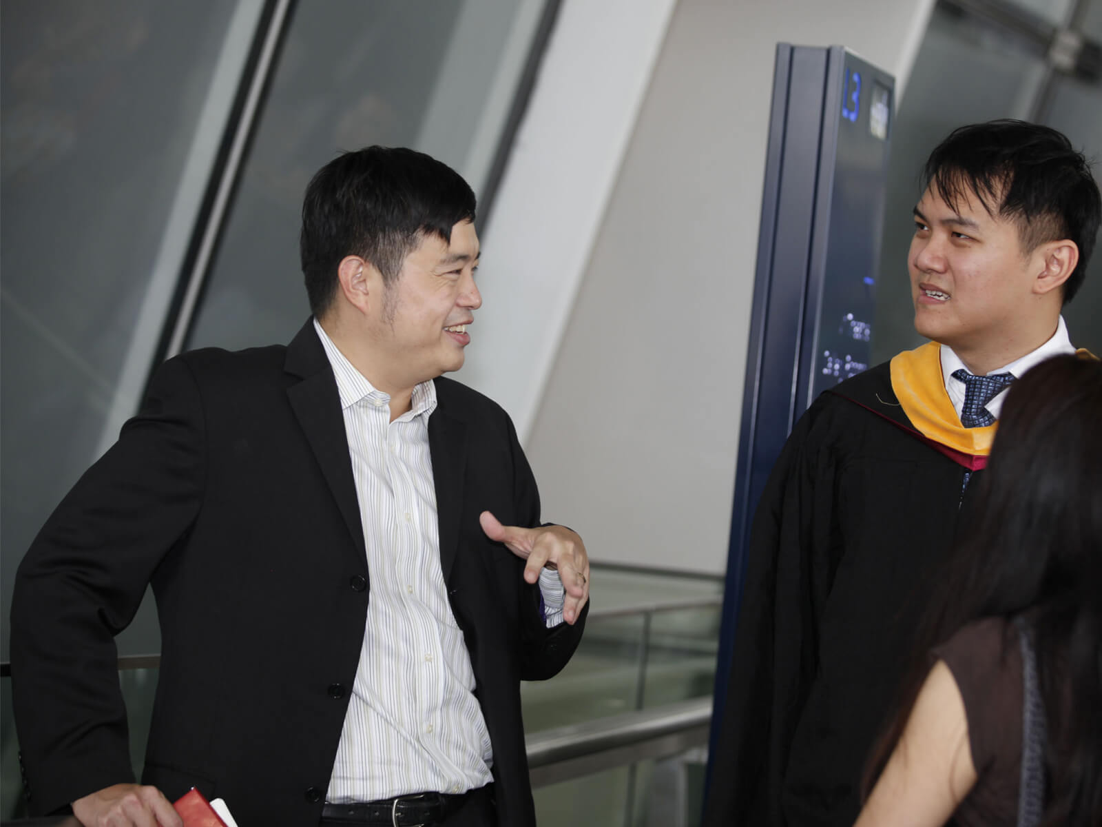 Dr. Edward Sim talks to a newly graduated DigiPen student who is wearing a cap and gown